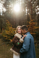 A man and a woman are hugging in the woods with sunlight on the background