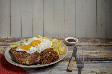 Bistec a lo pobre. beef, eggs, and french fries on a plate on a wooden table with cutlery. Typical Chilean food