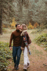 A woman is kissing a man on the cheek while walking through autumn forest, happy couple spending time together
