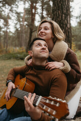 A man plays guitar and a woman hugs him from behind in autumn park outdoors
