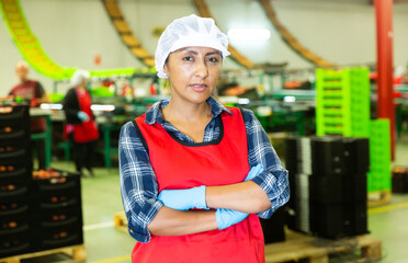 Portrait of female worker in uniform with arms crossed standing in fruit warehouse - 751825825