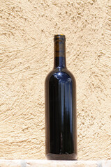 Portrait image of a generic bottle of red wine with reflection of sun and clouds on neutral beige plastered background. Selective focus