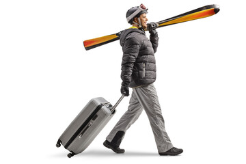 Full length profile shot of a man in winter coat carrying skiis and pulling a suitcase