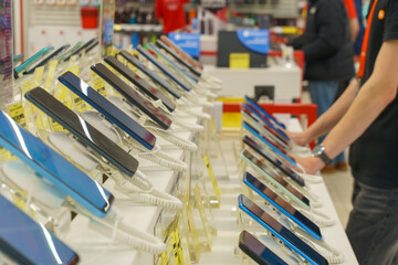 A showcase with a large number of modern mobile phones in an electronics store. Buy a mobile phone. Shoppers walk next to the smartphone shelf.