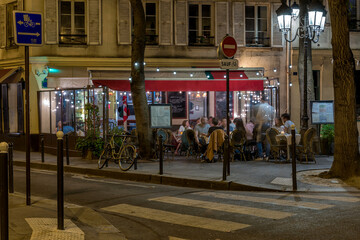 Cozy street with tables of cafe in Paris at night, France. Architecture and landmark of Paris. Paris cityscape