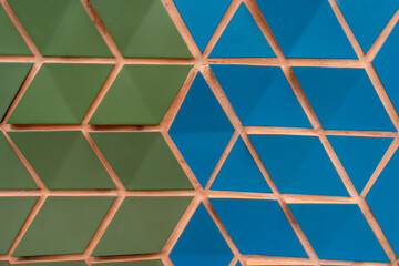 Geometric pattern composed of green and blue triangular tiles. Neatly arranged pieces forming large design. Thin terracotta-colored lines separating it