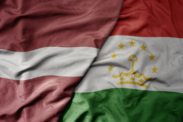 big waving national colorful flag of tajikistan and national flag of latvia.