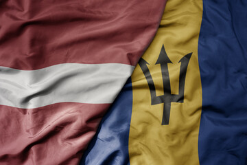 big waving national colorful flag of barbados and national flag of latvia.
