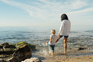 mother and son go into the sea. mother and son test the water with bare feet. mother and son having...