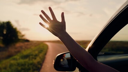 Girl with long hair sits in front seat of car, her hand out window and catching wind, glare of...