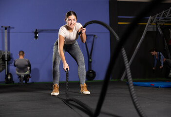 Powerful fitness girl training with black battle ropes crossfit at indoor