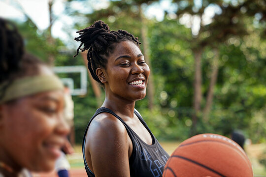 Candid moment of African American young women laughing together on a basketball court, symbolizing friendship and joy.

