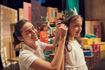 A young female teacher assists a female student in dressing up for a school play, capturing a candid moment of everyday educational life.

