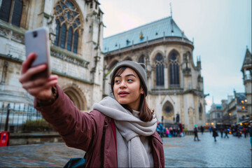 Gen Z Asian female tourist capturing a selfie with the grand backdrop of a European cathedral, embodying the spirit of travel.

