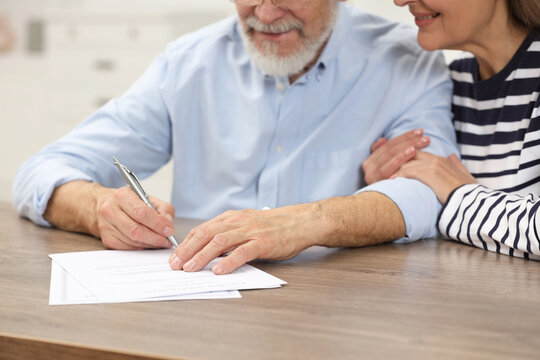 Happy senior couple signing Last Will and Testament at wooden table, closeup