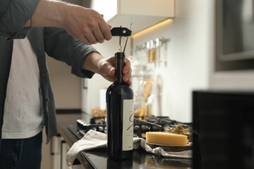 Man opening wine bottle with corkscrew at black countertop indoors, closeup