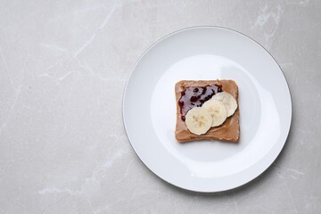 Toast with tasty nut butter, jam and banana on light table, top view. Space for text