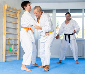 Young man and elderly man judokas practicing judo fight in gym