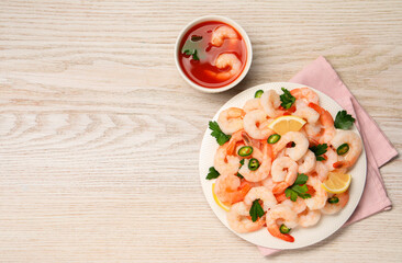 Tasty boiled shrimps with cocktail sauce, chili, parsley and lemon on light wooden table, flat lay. Space for text