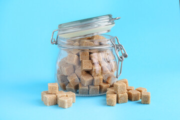Brown sugar cubes in glass jar on light blue background