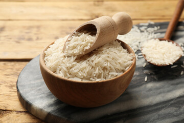 Raw basmati rice in bowl, scoop and spoon on wooden table, closeup
