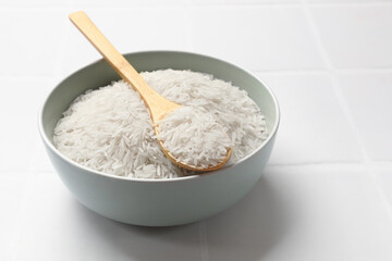 Fototapeta na wymiar Raw basmati rice in bowl and spoon on white tiled table