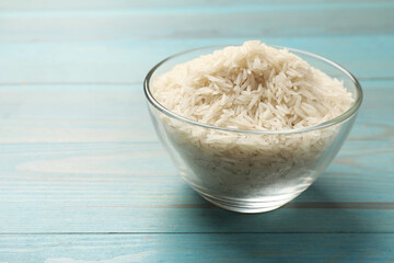 Raw basmati rice in bowl on light blue wooden table, space for text