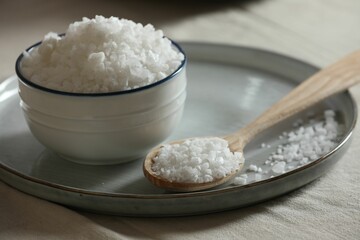 Organic salt in bowl and wooden spoon on table, closeup