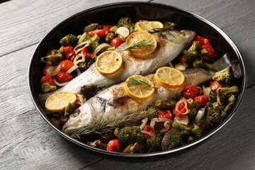 Baked fish with vegetables, rosemary and lemon on grey wooden table, closeup
