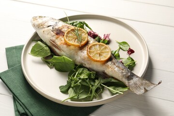 Baked fish with spinach and lemon on white wooden table, closeup