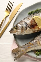 Delicious baked fish served on white wooden table, top view