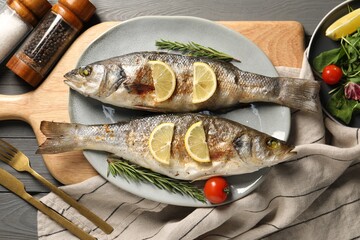 Delicious baked fish served on grey wooden table, top view