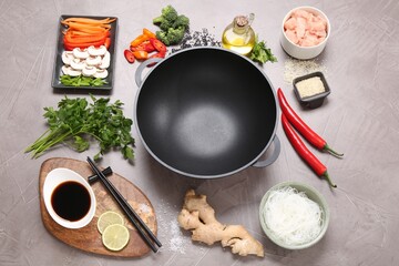 Wok, chopsticks and different products on grey textured table, above view