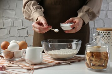 Woman with spoon and bowl of baking powder at white wooden table, closeup