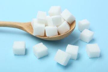 White sugar cubes and wooden spoon on light blue background, closeup