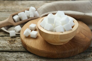 Fototapeta na wymiar White sugar cubes in bowl and scoop on wooden table, closeup