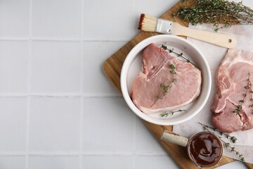 Raw meat, thyme, basting brush and marinade on white tiled table, top view. Space for text