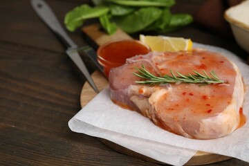 Board with raw marinated meat and rosemary on wooden table, closeup. Space for text