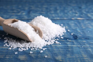Natural salt and scoop on blue wooden table, closeup. Space for text