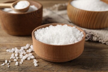 Fototapeta na wymiar Natural salt in different dishware on wooden table, closeup