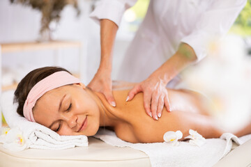 Young woman relaxing on massage table while skilled therapist delivering soothing Swedish back and shoulders massage, promoting stress relief and muscle relaxation