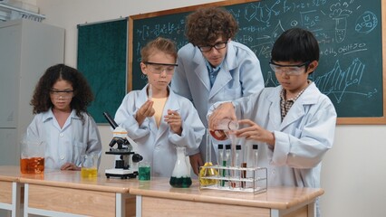 Children doing experiment in science lesson while standing at blackboard at laboratory. Happy student discovering and learning about biochemical liquid while inspecting and mixing sample. Pedagogy.