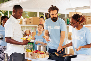 Humanitarians distribute warm meals to needy individuals through non-profit organization. Hunger relief volunteers smiling while sharing free food and necessities at food drive to homeless people.