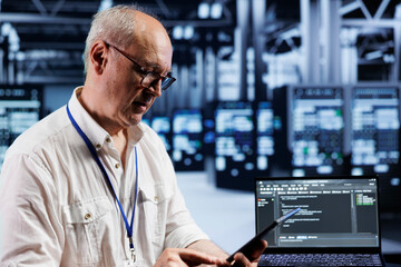 Aged precise engineer coding in technologically advanced data center using javascript language. Expert updating software on server racks on laptop terminal, ensuring errorless performance and security