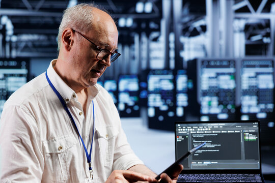 Aged precise engineer coding in technologically advanced data center using javascript language. Expert updating software on server racks on laptop terminal, ensuring errorless performance and security - Powered by Adobe