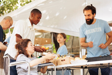 Poor caucasian female wheelchair user receives free food and nourishments at outdoor food bank....