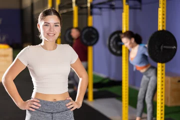 Behang Cheerful girl in sportswear standing and posing in gym © JackF