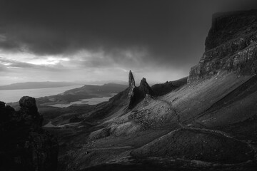 Atmospheric view of high sharp cliffs towering over the lakes and sea, and the looming rain cloud at sunrise. The Old Man of Storr before the rain in black and white. The Isle of Skye, Scotland, UK