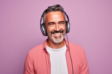 Portrait of a happy mature man listening to music on headphones and smiling while standing against...