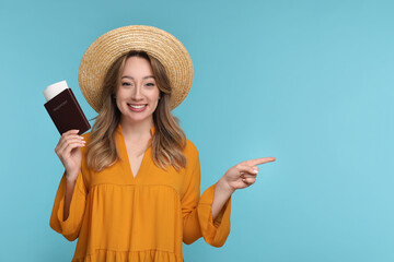Happy young woman with passport, ticket and hat pointing at something on light blue background,...